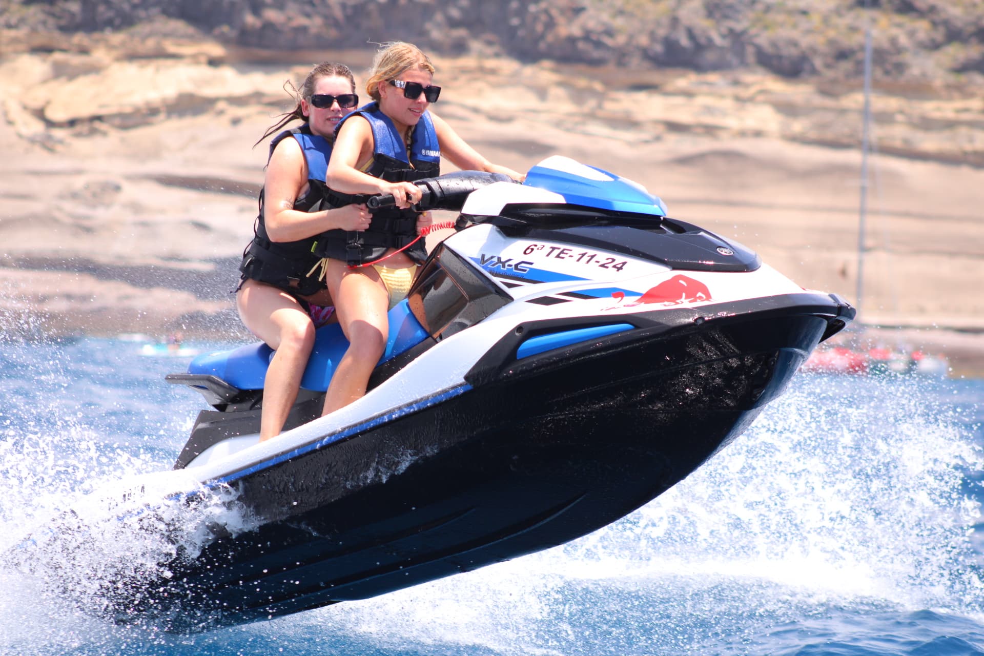 Chicas sonriendo en moto de agua frente a la costa
