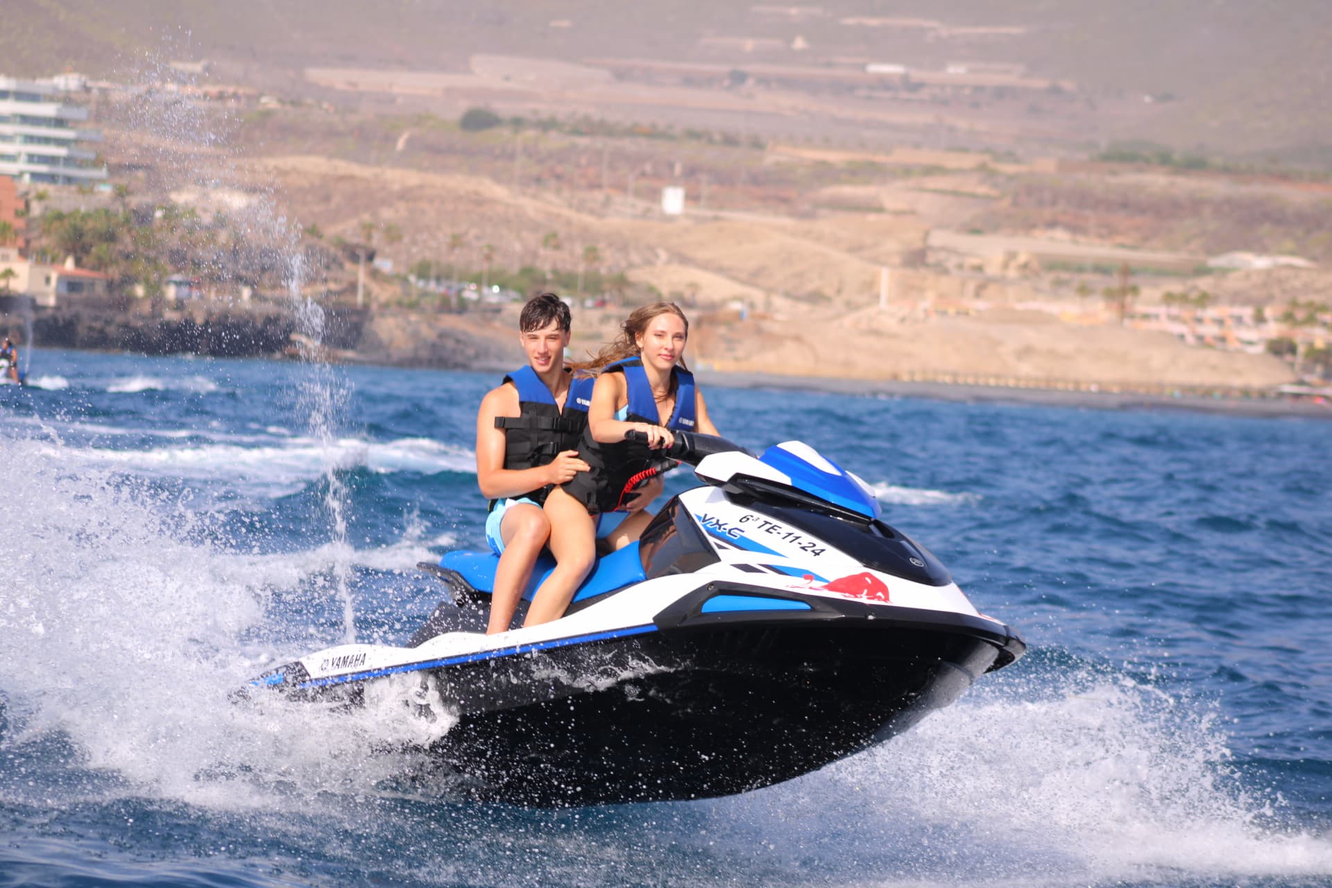 Pareja joven en jet ski con la costa de fondo